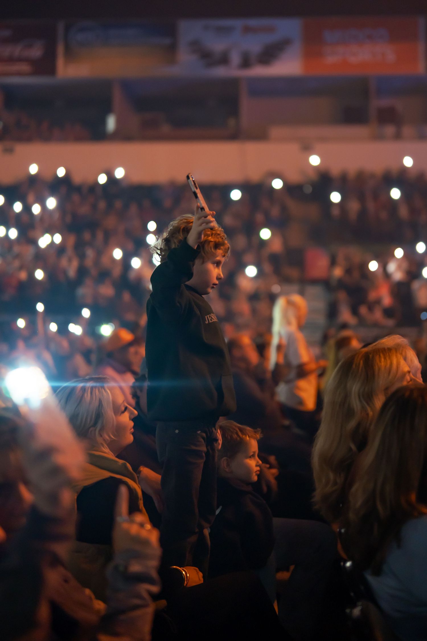 Concert audience silhouettes with glowing lights and raised hands during worship performance.