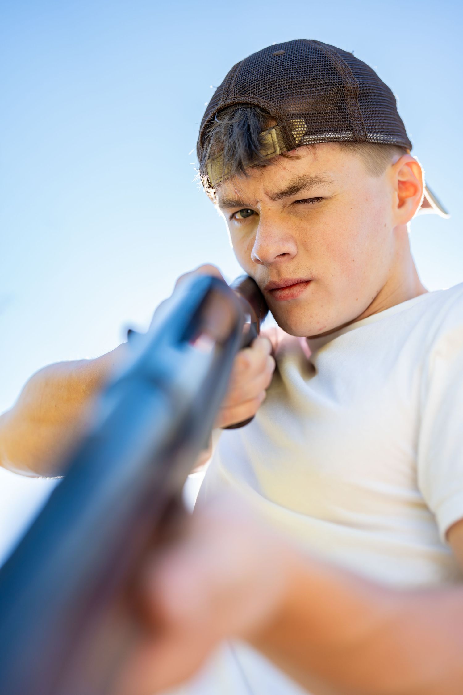 Close-up profile view of someone wearing a black baseball cap against a bright blue sky background.