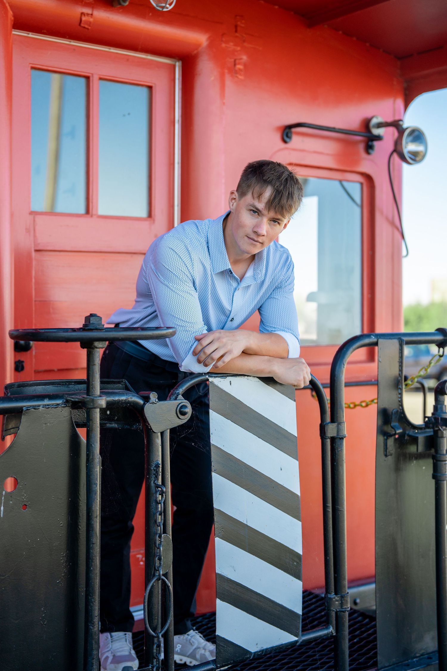 Someone in business casual attire posing on a vintage red train car platform.