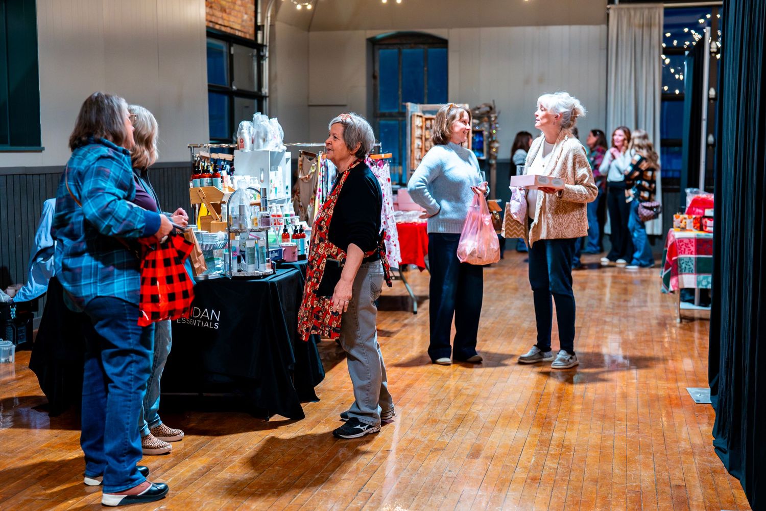 Wide view of an indoor market space with vendors and shoppers on hardwood floors.