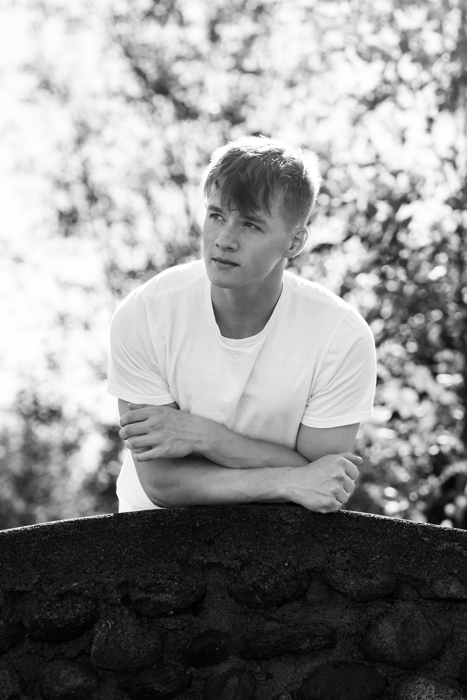 Black and white portrait of someone resting on stone wall outdoors.