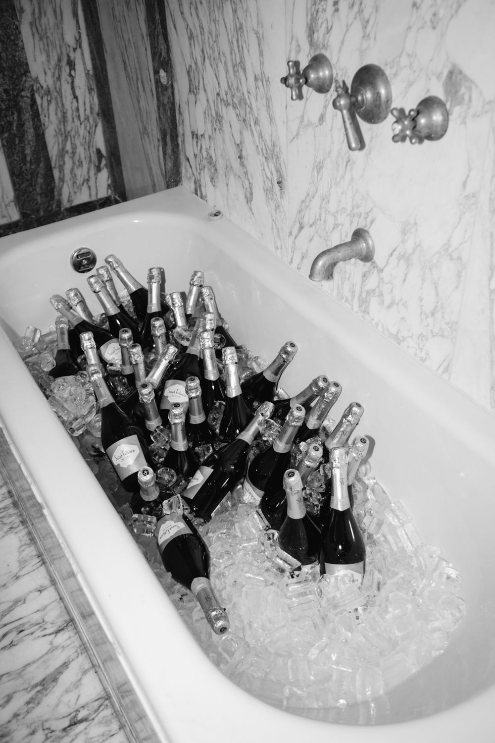 Bathtub filled with champagne bottles on ice in a marble bathroom, black and white photo.