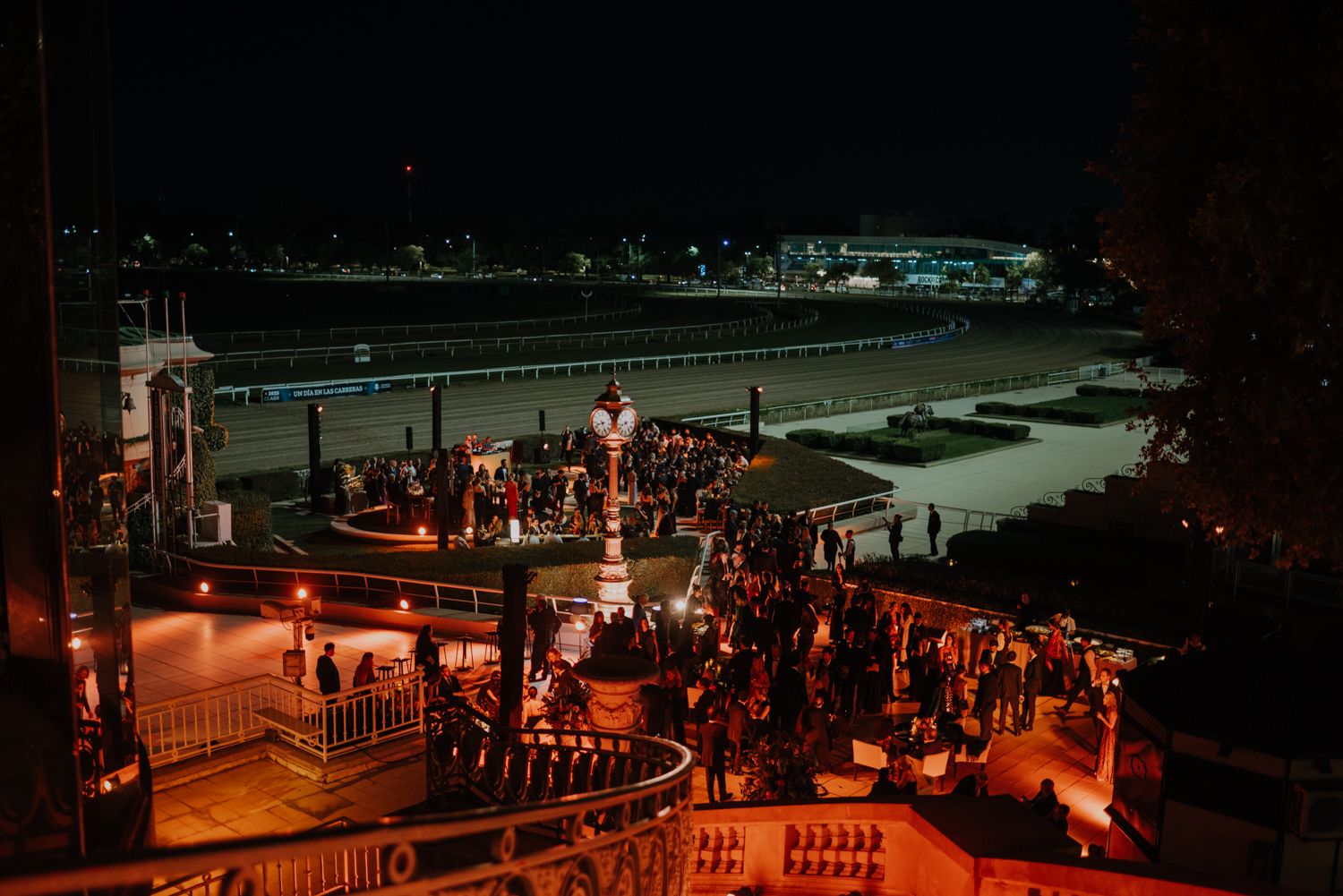 Elegant outdoor evening wedding reception venue overlooking racetrack with warm ambient lighting.