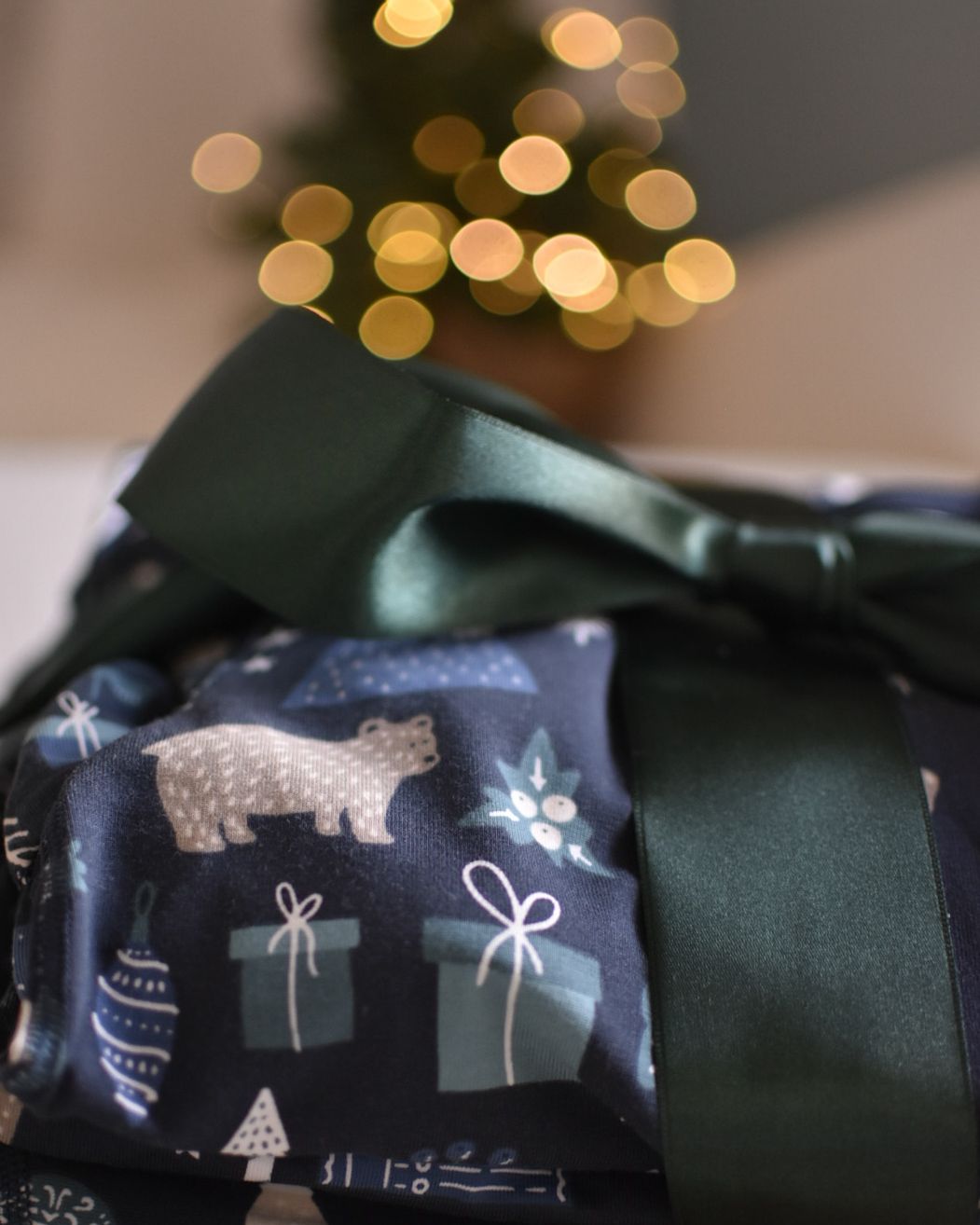 Christmas pyjamas wrapped with a green bow in front of bokeh effect Christmas lights