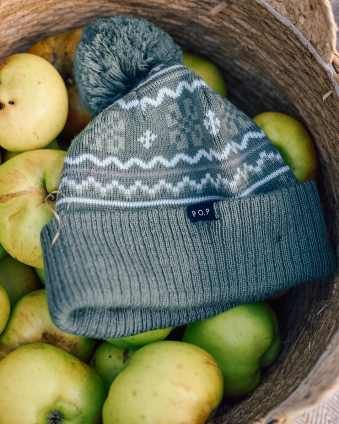 Green wooly hat in a wicker basket with a pile of green cooking apples