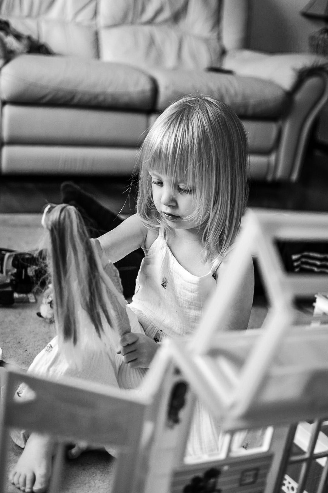 Girl playing with barbie doll with sofa in background. Black and white photo