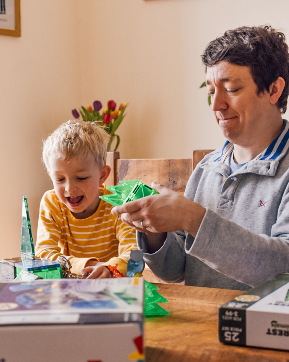 Man and boy sat at wooden dining table playing with Magna Tiles