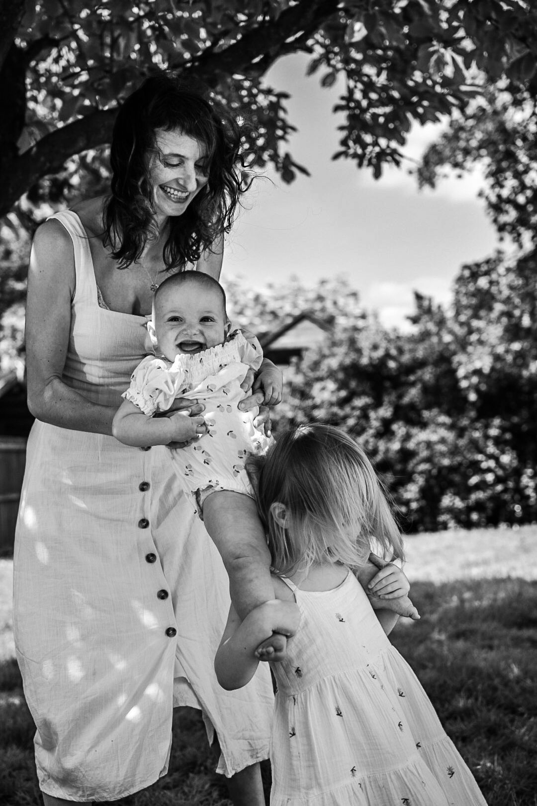 Black and white photo of mother holding a baby under arms whilst girl holds legs in front.
