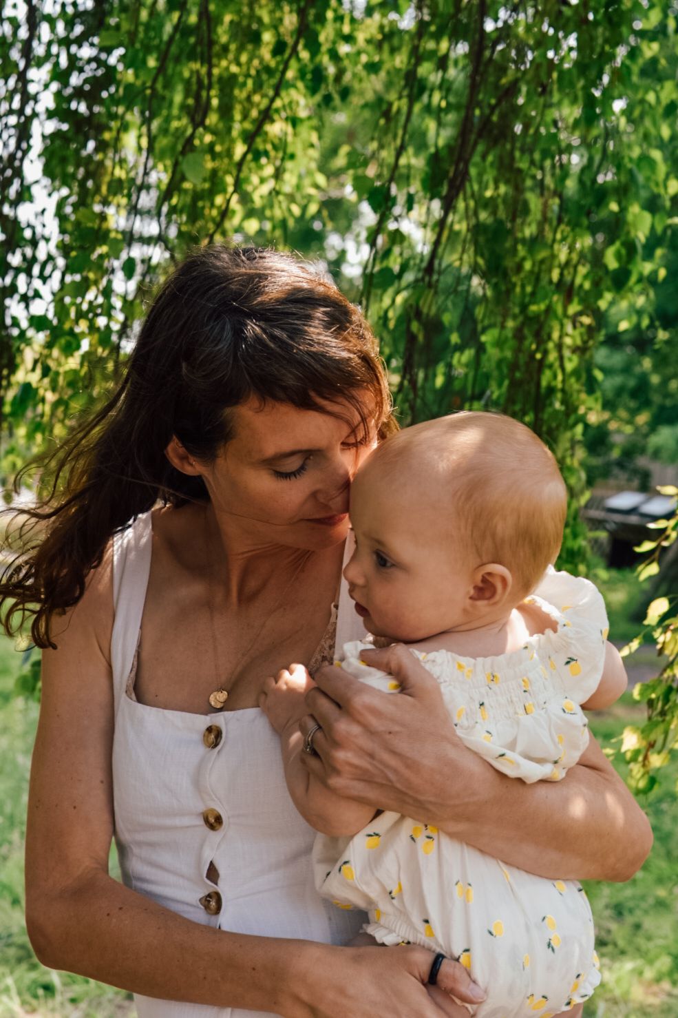 Mother and Baby embrace in garden scene with trees in background