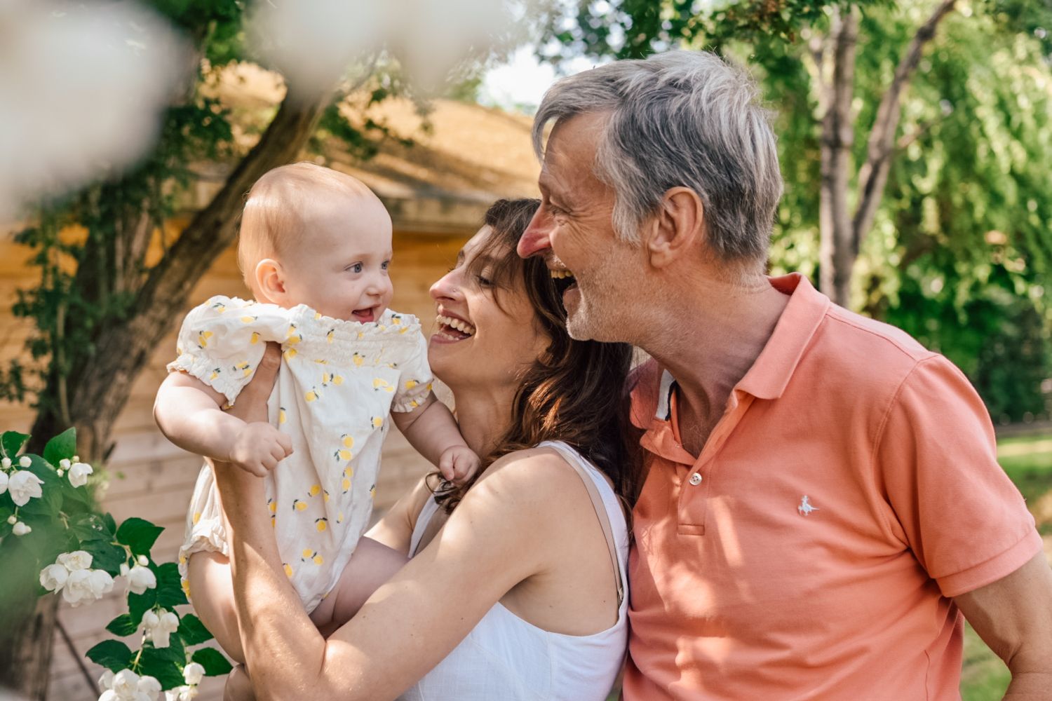Mother holding baby aloft with grandfather behind her smiling at baby in garden scene