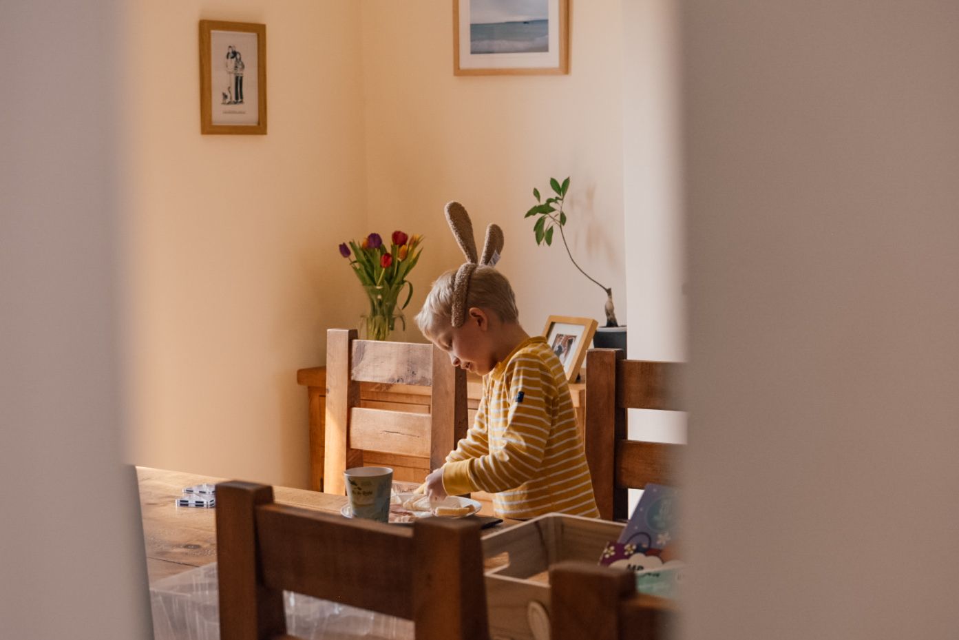 Boy kneeling on a chair at wooden dining table playing with Magna Tiles