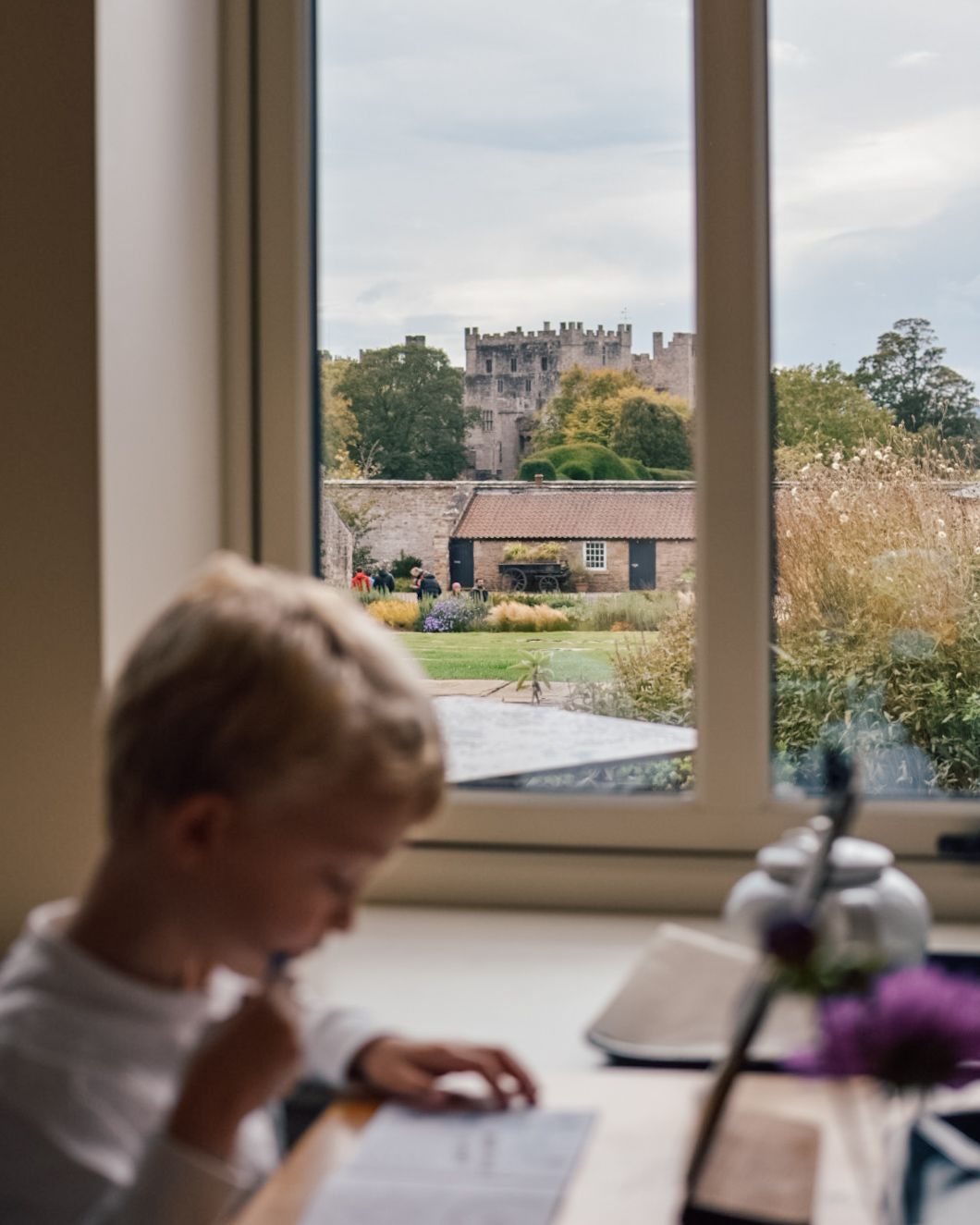 Boy looking at vinery food menu sat at a table by a window with Raby Castle visible in the background.