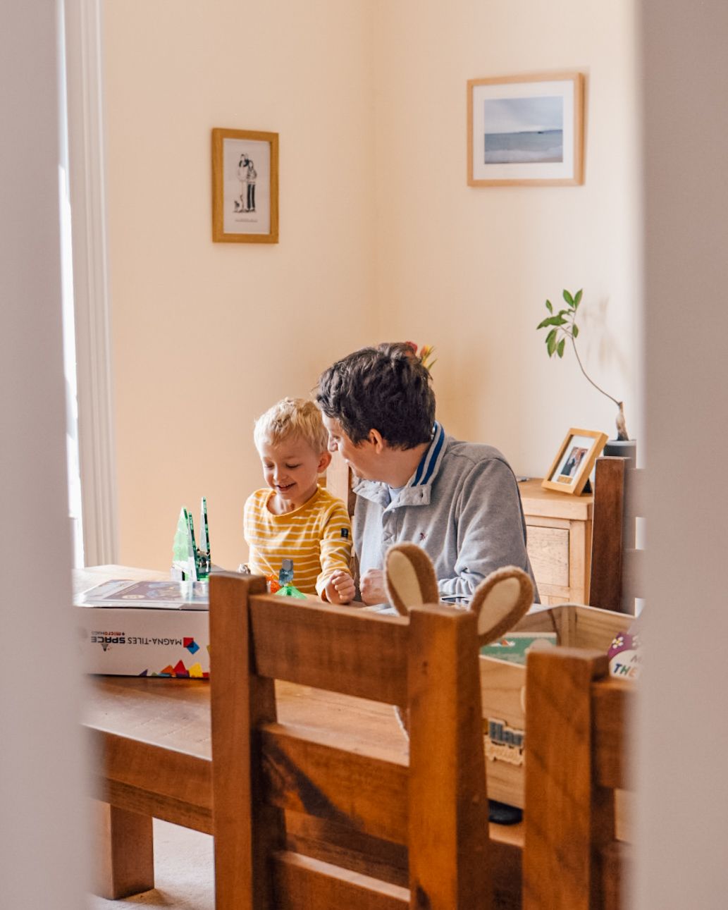 Man and boy sat at wooden dining table playing with Magna Tiles
