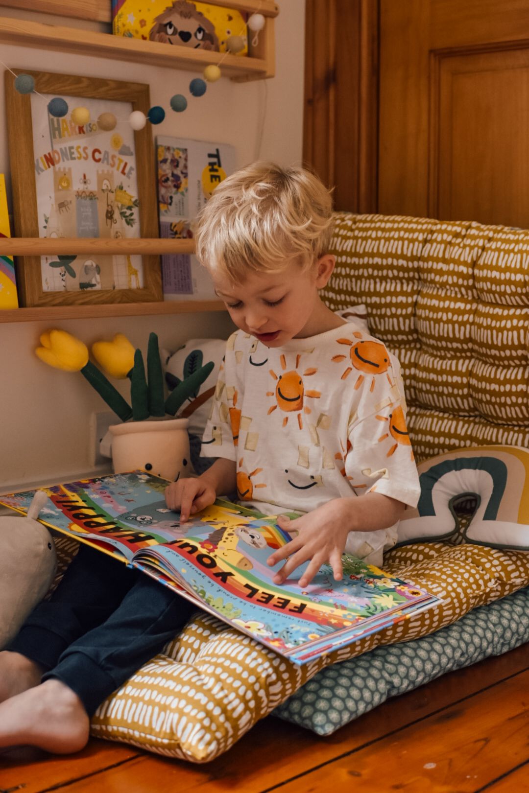 Boy reading feel your happy book by Emily Coxhead on a floor cushion in a reading corner next to bookcases on the wall