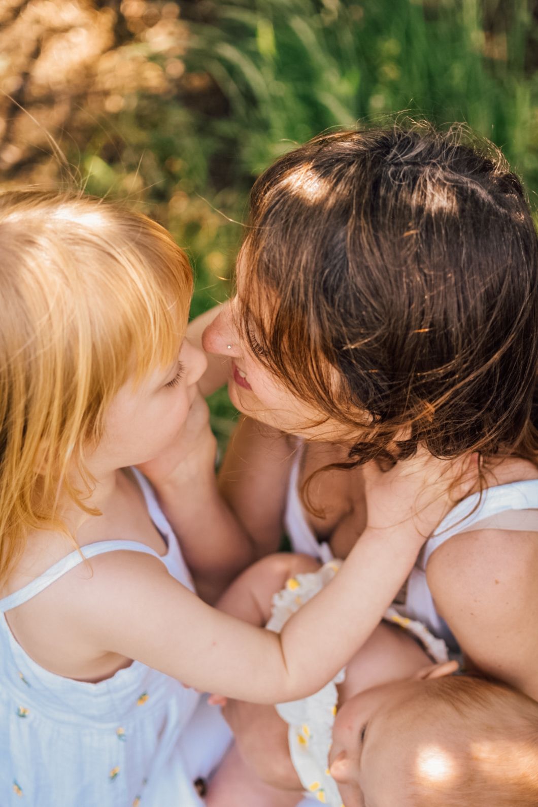 Mother holding a baby embraces with girl in garden photo