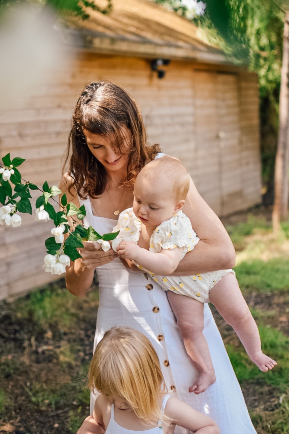 Mother holding a baby looking at blossom on a tree with girl walking in front of them
