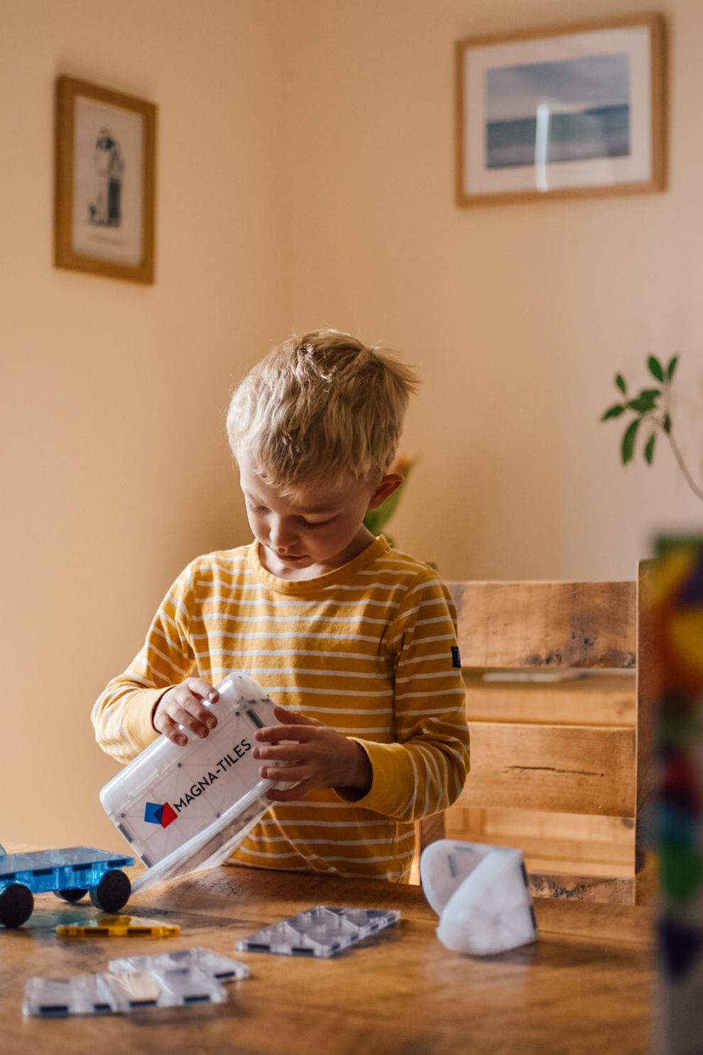 Boy playing with magna tiles space ship product on a wooden table sat at a wooden chair with a wooden sideboard in the background