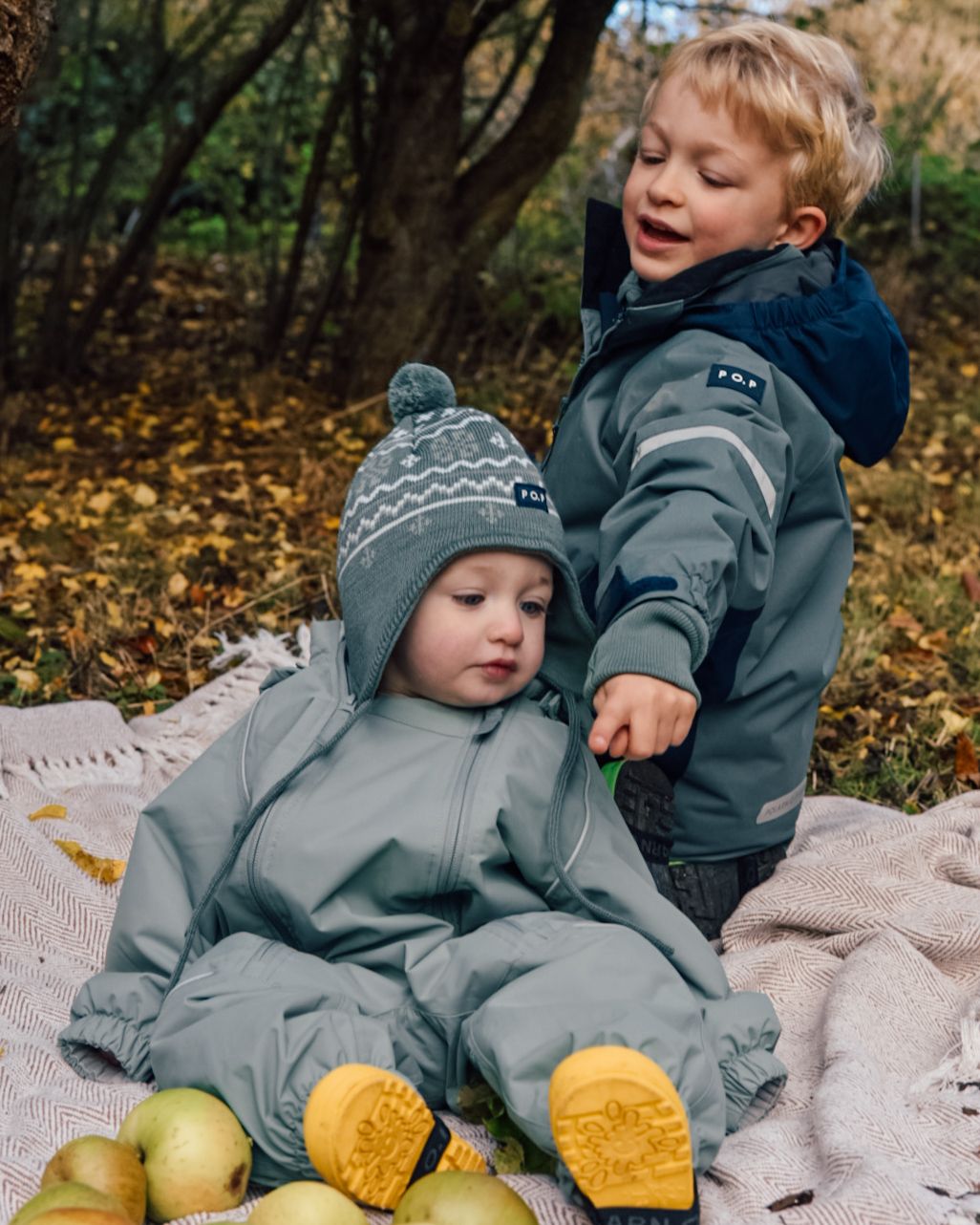Baby and boy sat on a blanket in woodland area looking at apples