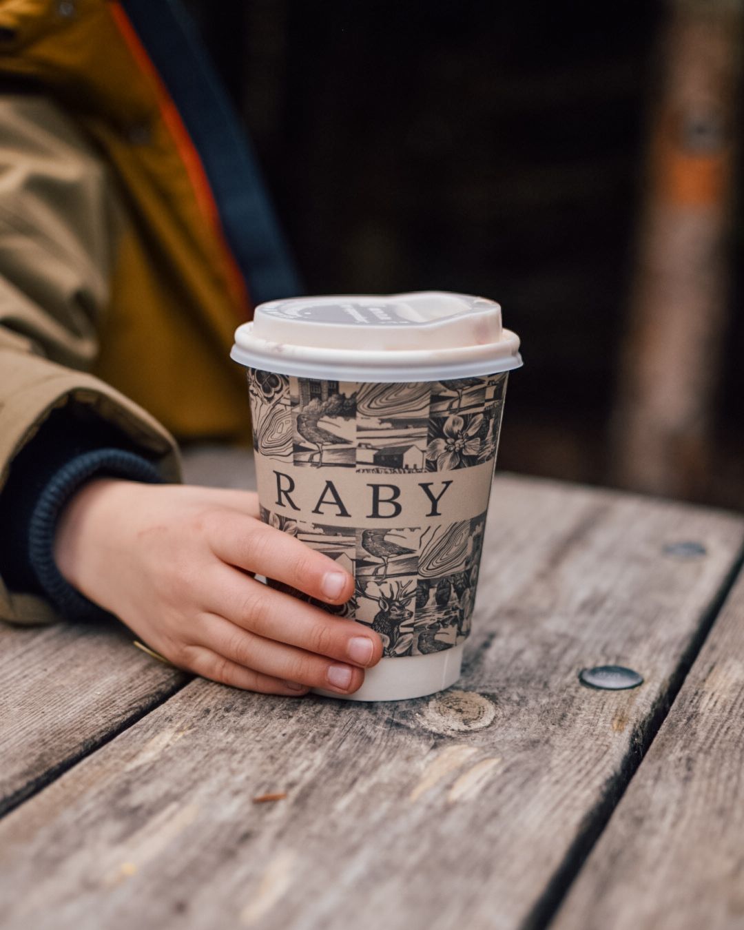 Small hand holding a Raby Castle branded paper cup