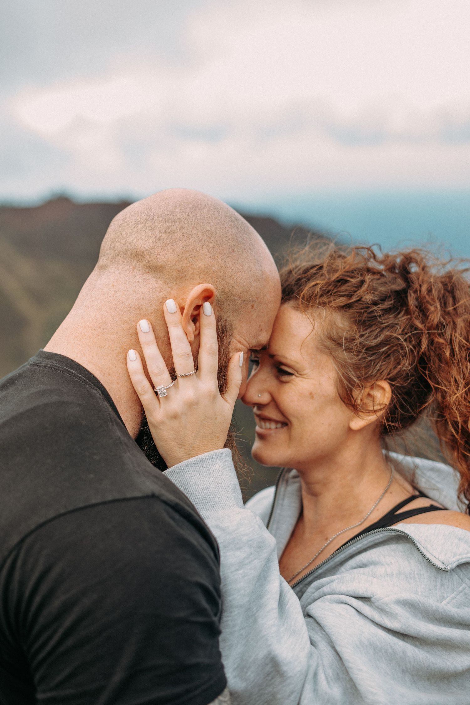 Kaua‘i engagement photoshoot on the Nā Pali Coast featuring a couple embracing at sunset with ocean views, tropical cliffs, and  beach