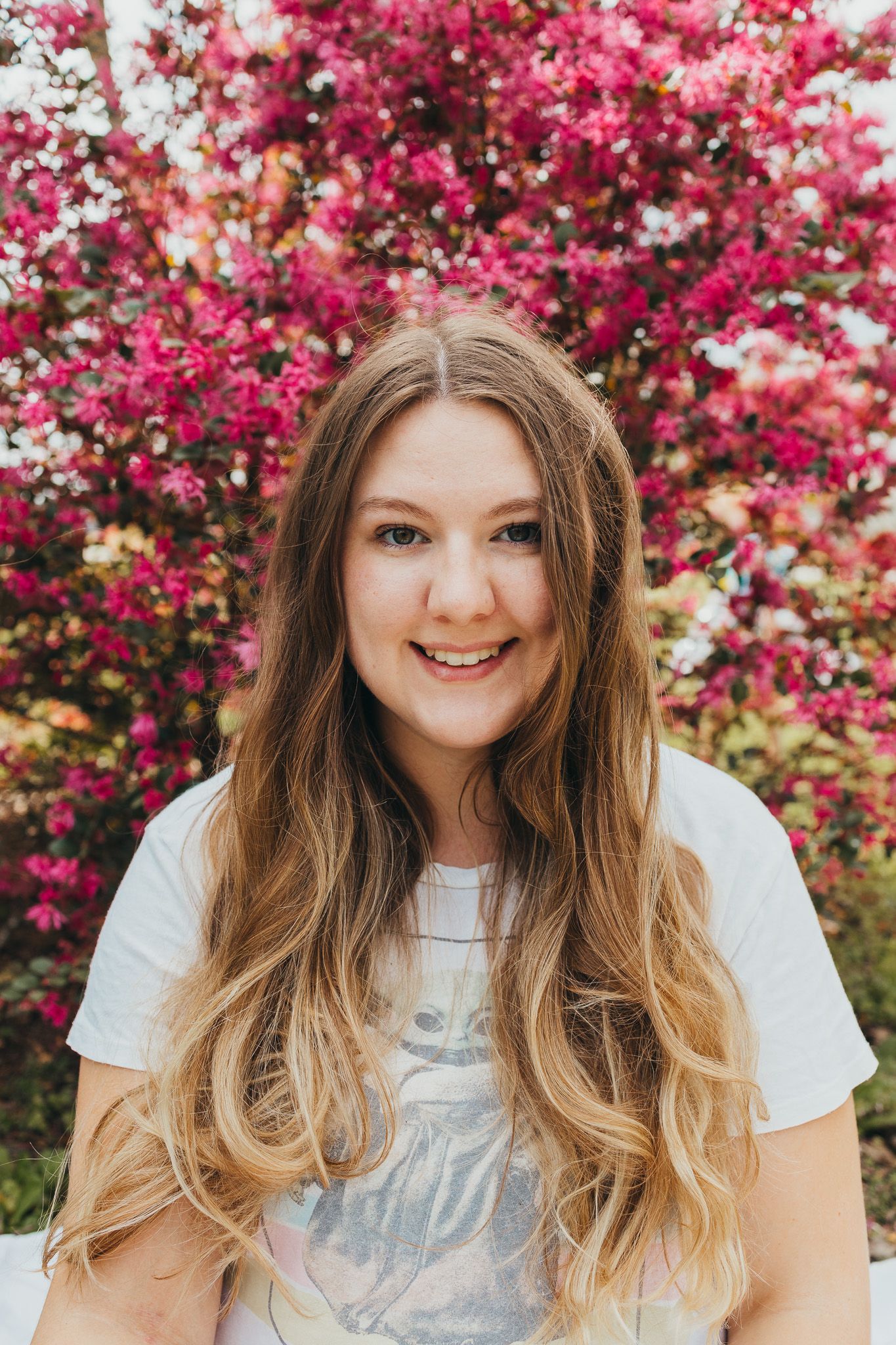 A person in a white t-shirt poses against vibrant pink flowering trees in a spring portrait series.