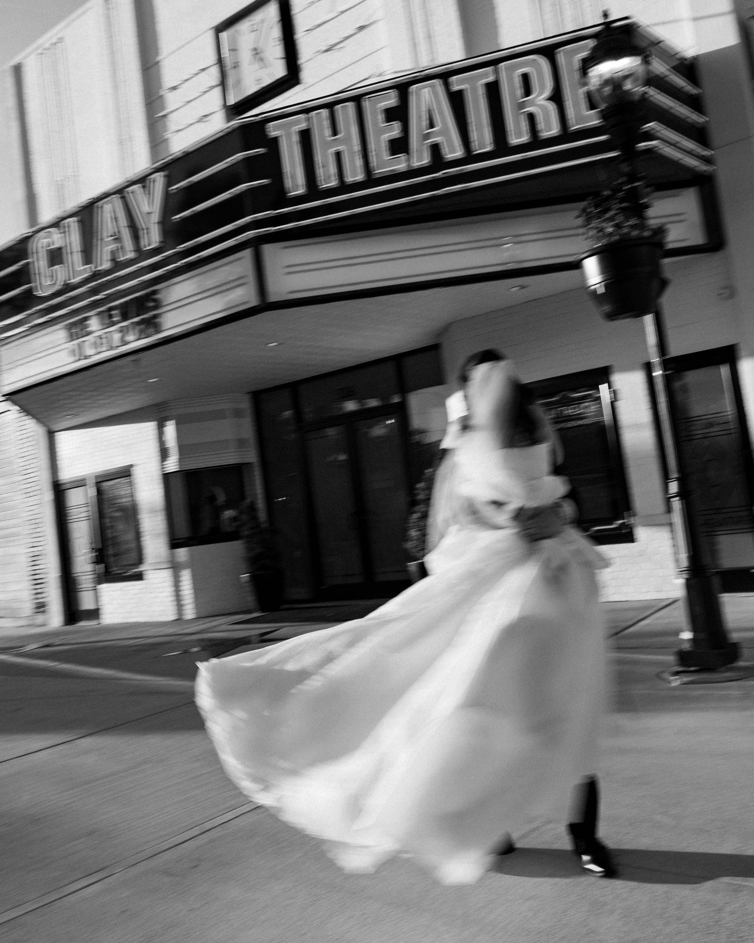 Black and white motion shot of a bride dancing outside a vintage theater building.