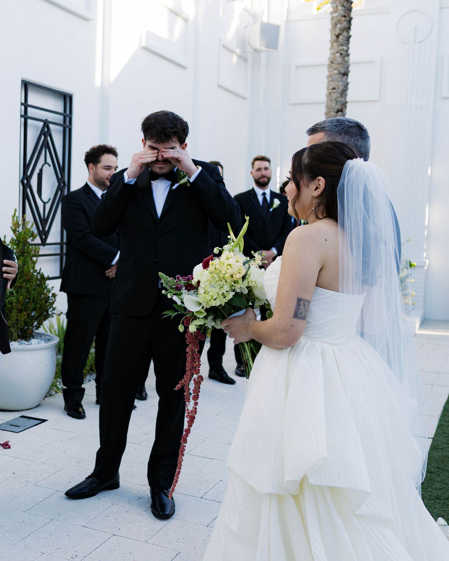 An intimate wedding ceremony moment captured against a white architectural backdrop.