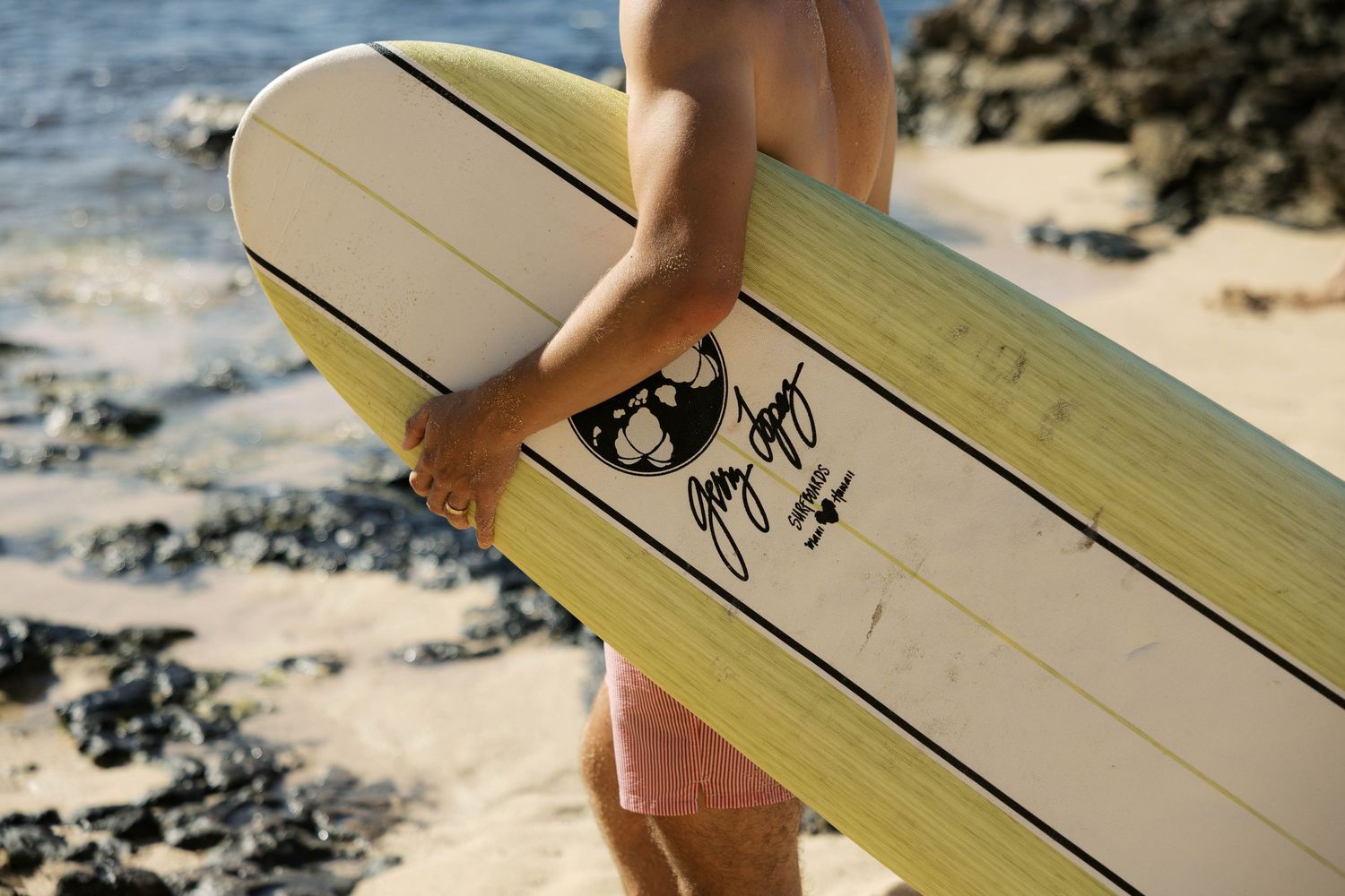 Close-up of white surfboard with black graphic design on beach.