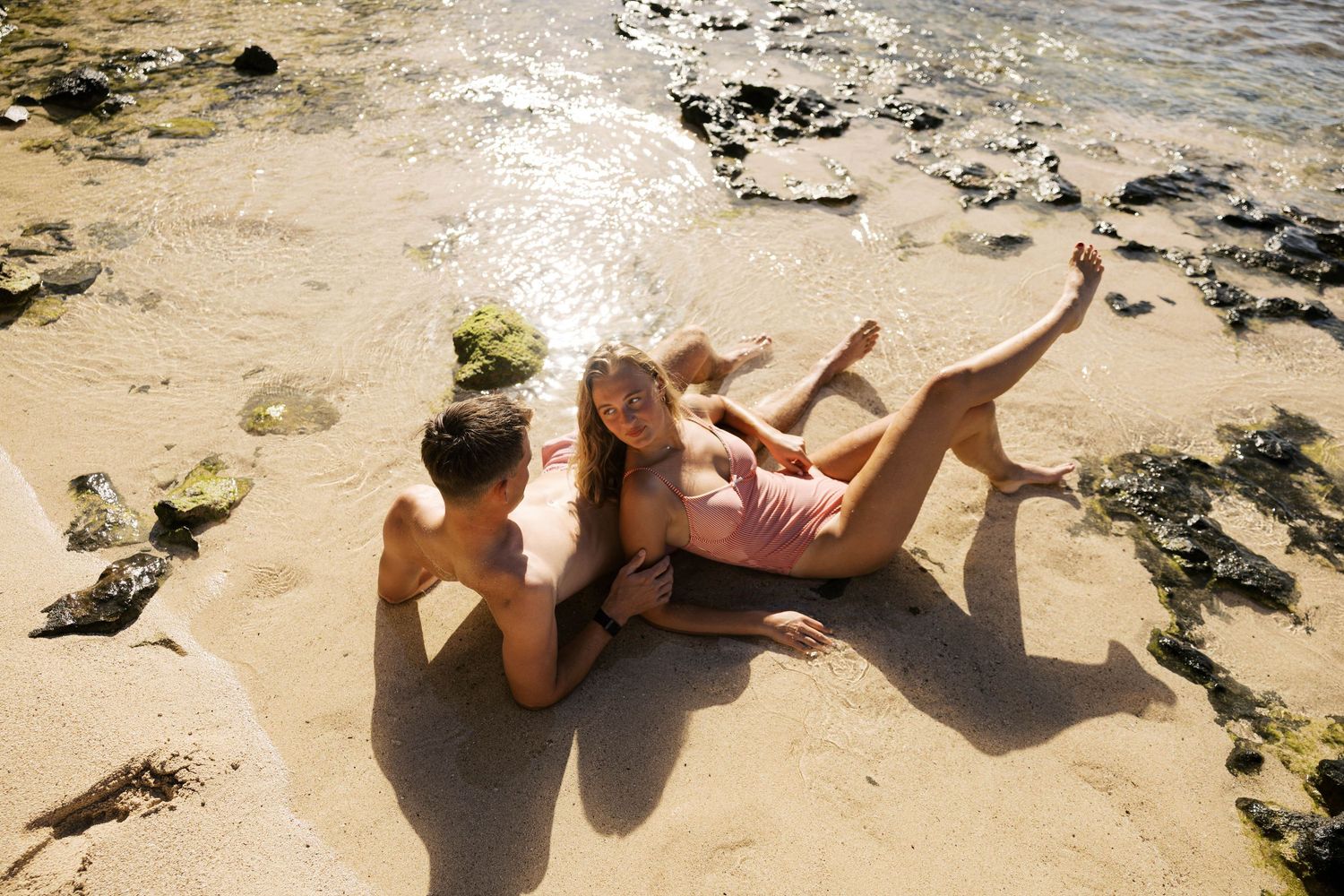 Couple relaxing on rocky beach shore during sunny day.