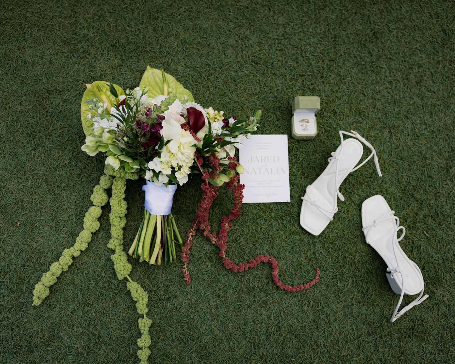 Wedding florals and decor elements artistically arranged on green textured surface.