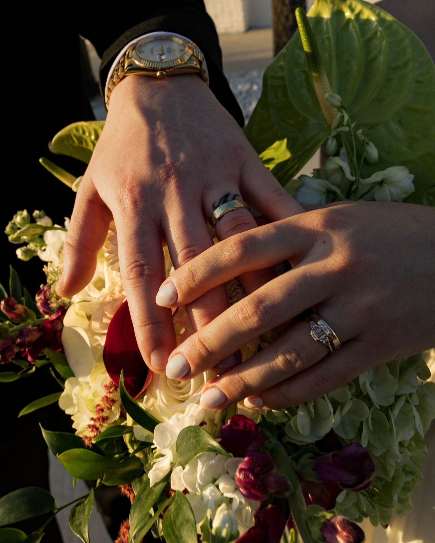 Close-up of hands holding a white and red floral wedding bouquet in natural lighting.