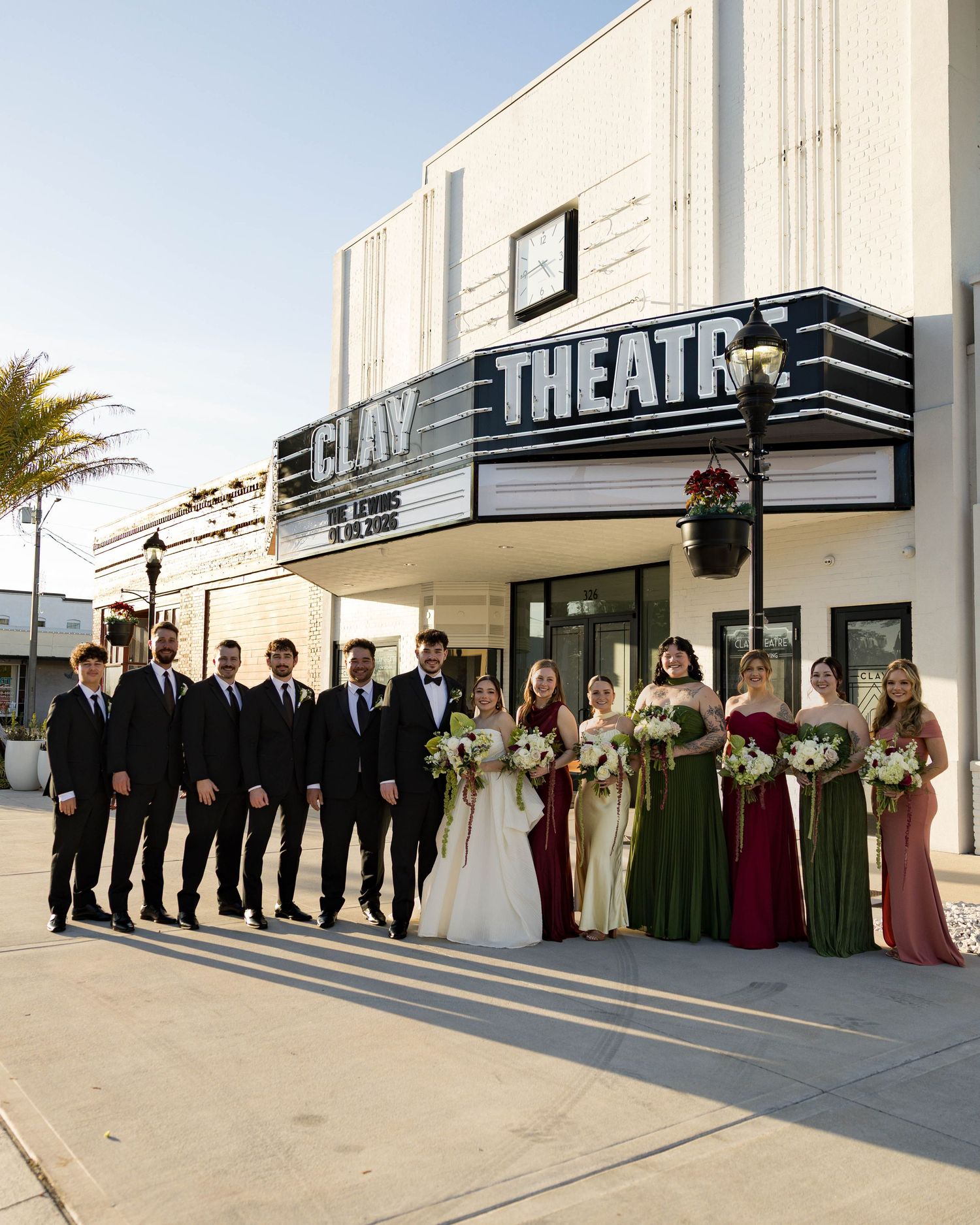 Wedding party poses outside vintage theatre building with art deco signage.