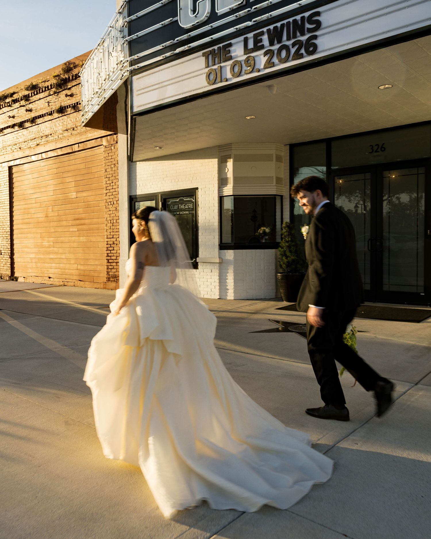 A bride's dress flows beautifully as the newlyweds walk along the Clay Theatre sidewalk.