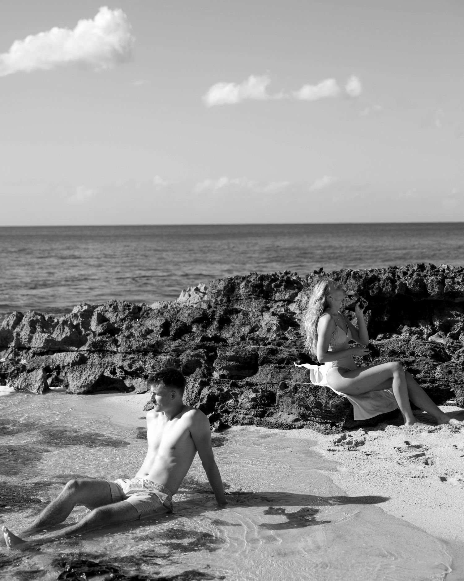 Black and white photo series of a person relaxing on a beach near rocky coastline.