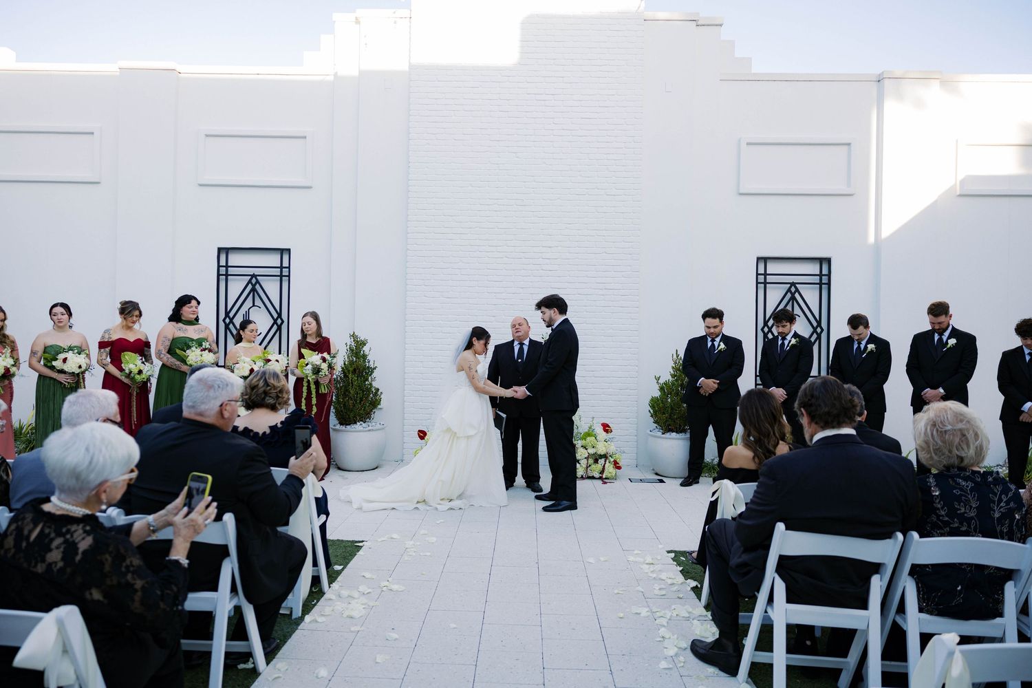 Wedding ceremony setup with white chairs and guests watching the couple exchange vows.