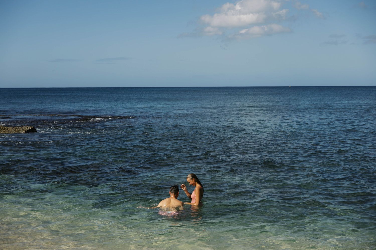 Two people swimming in clear turquoise ocean waters near rocky shore.