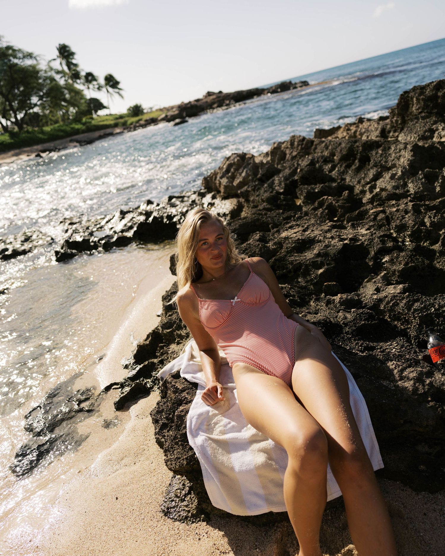 Person in beachwear posing on sandy shore with volcanic rocks and ocean waves.