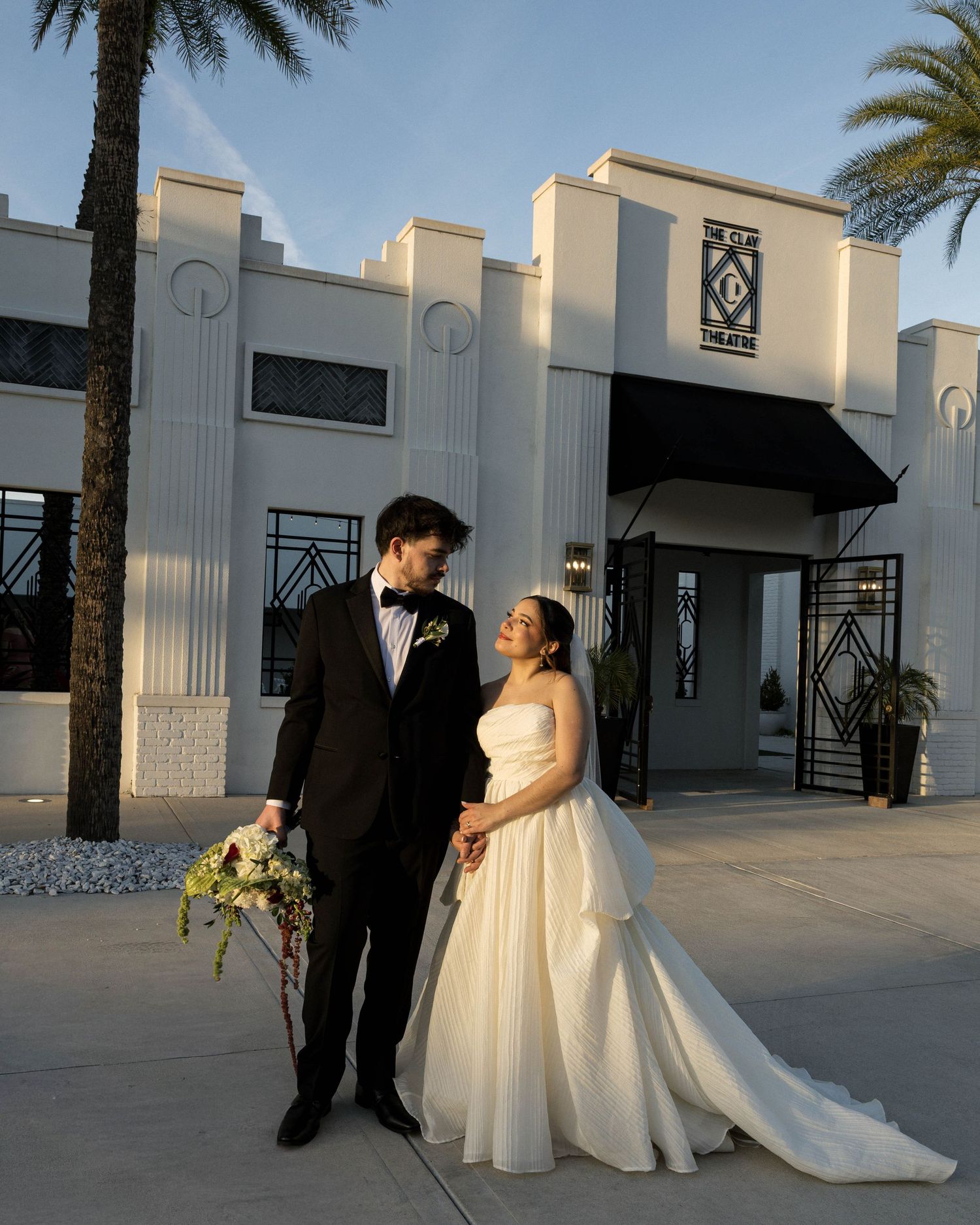 Wedding couple poses outside modern white building with palm trees.
