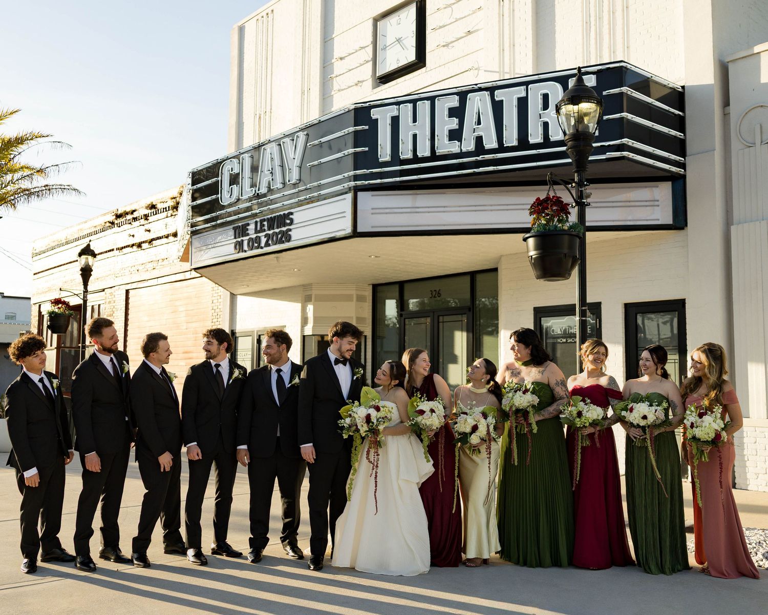 Bridal party and groomsmen line up for formal photos in front of classic theatre marquee.