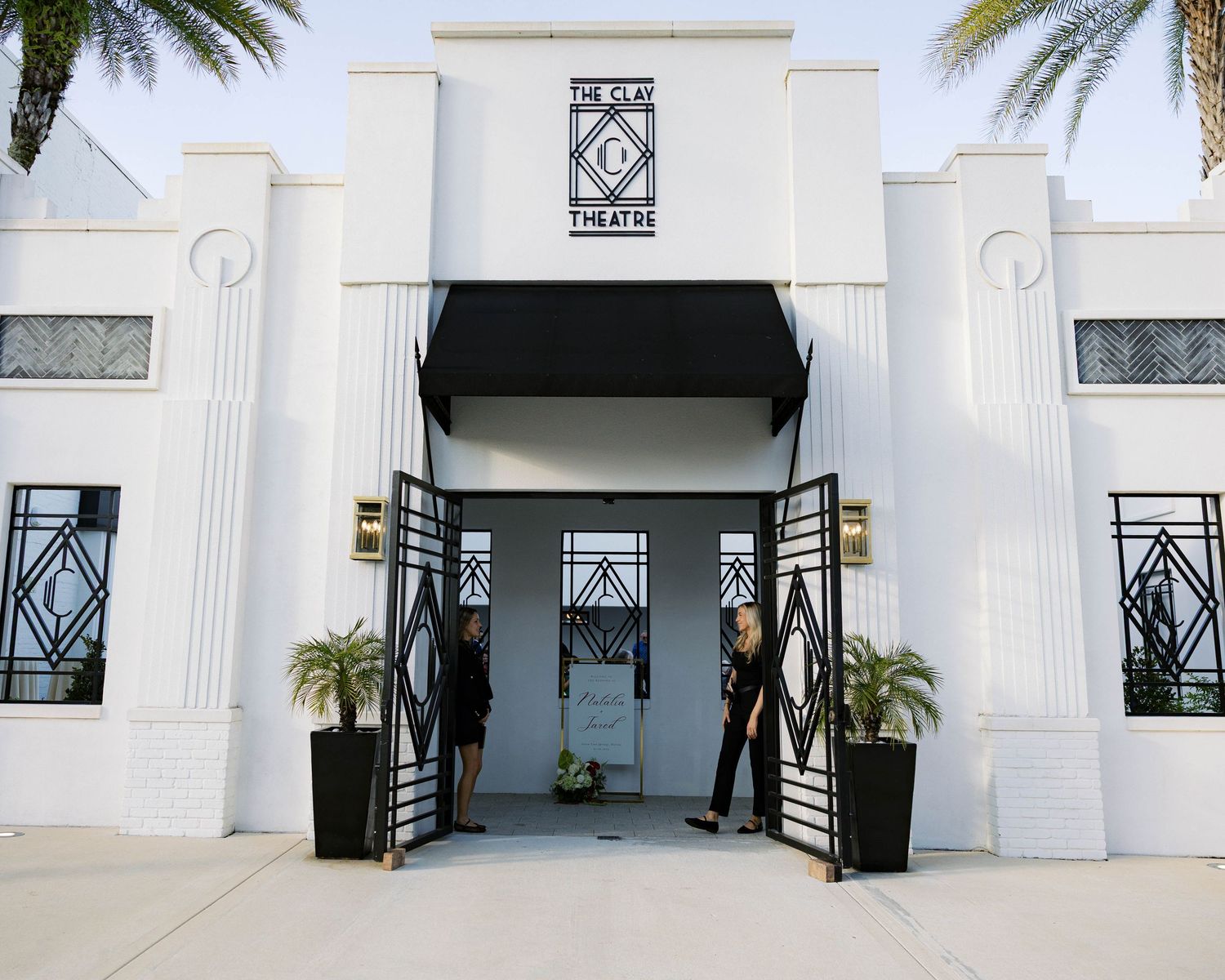 Modern white art deco style building entrance with geometric patterns and palm trees.
