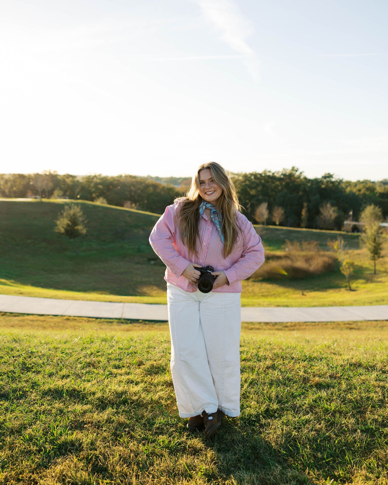 A person in a white coat stands in a grassy field during golden hour sunset lighting.