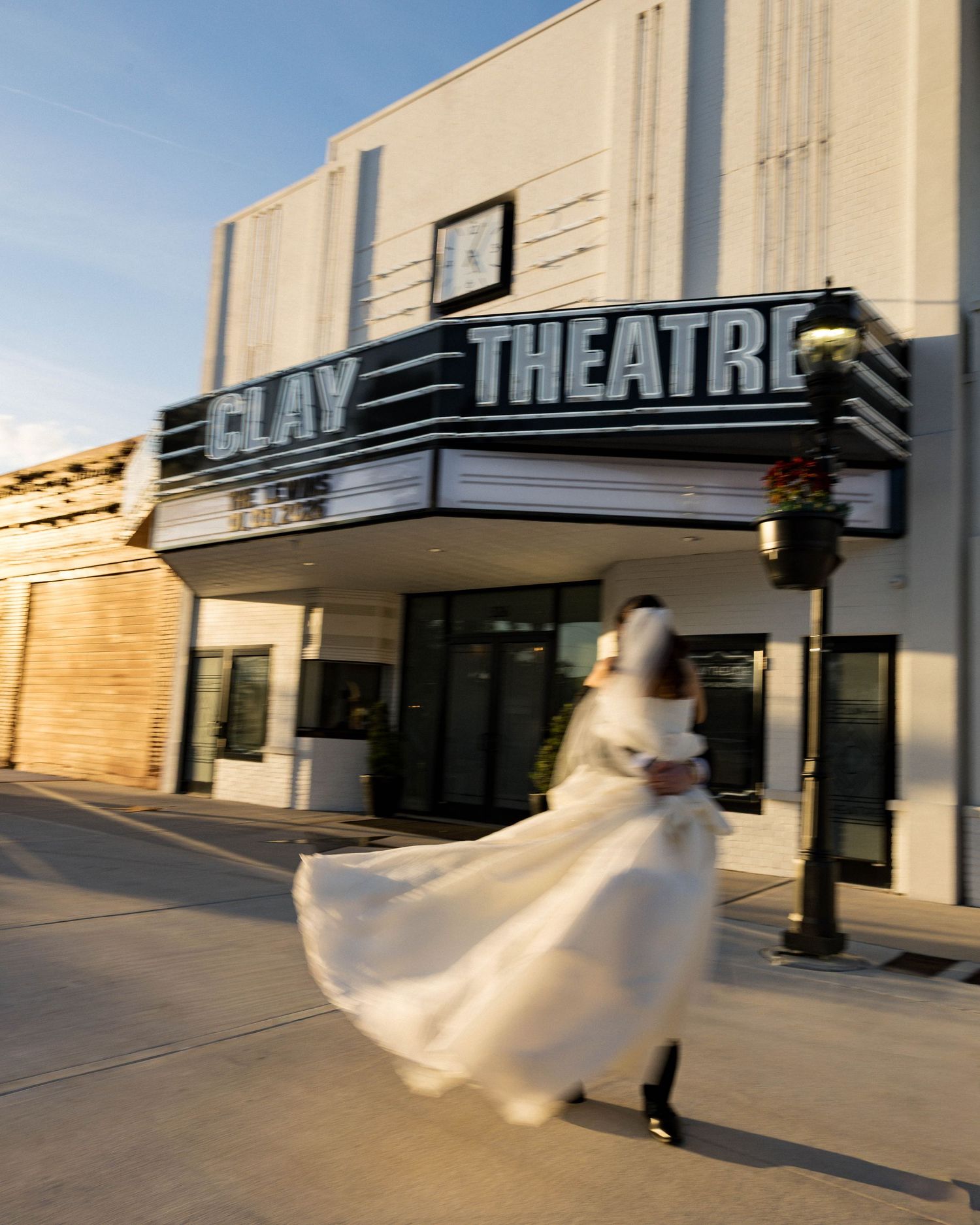 Motion-blur photo of a bride twirling in her wedding dress outside a theater entrance.