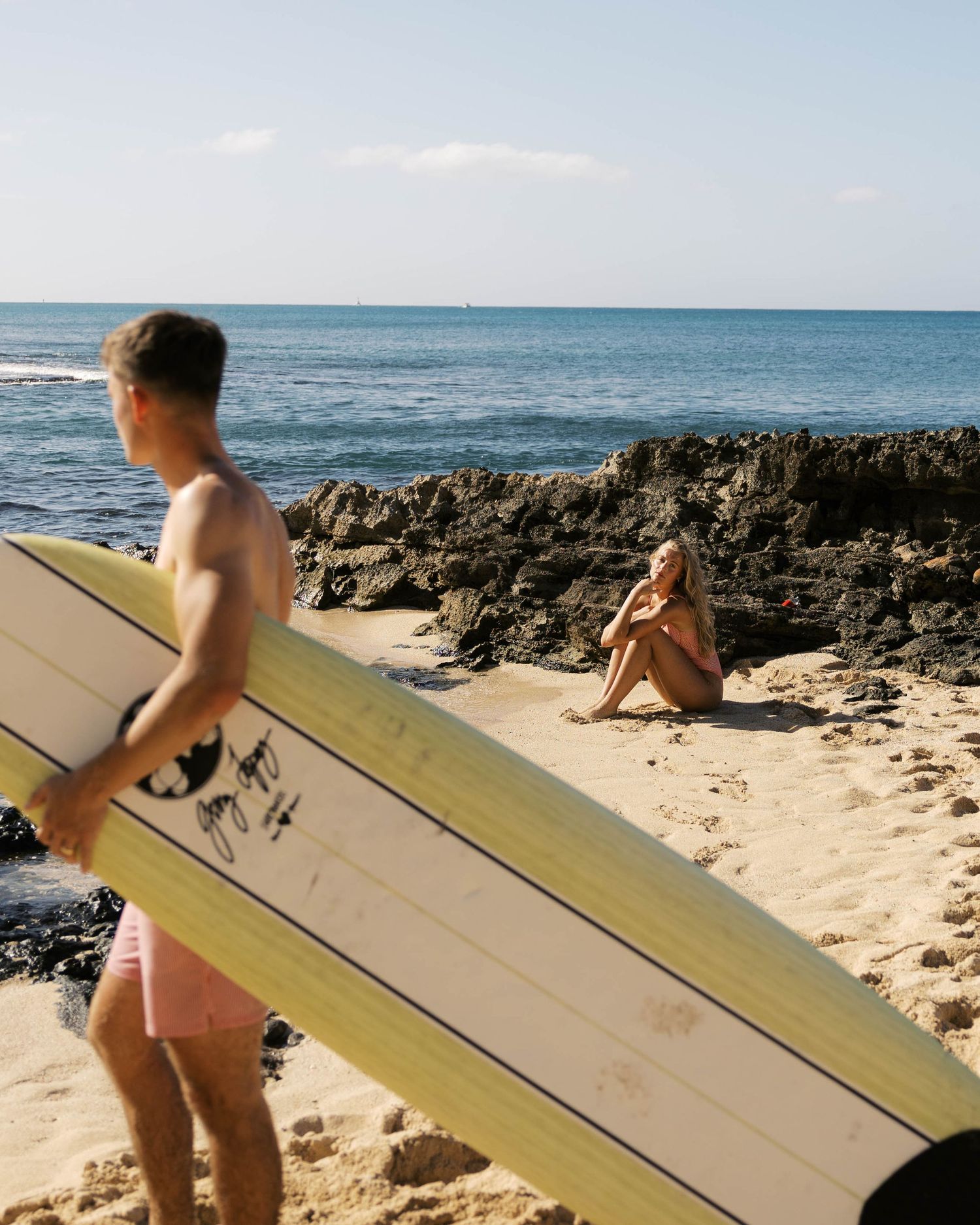 Surfers walking with longboard on tropical beach with volcanic rock formations.
