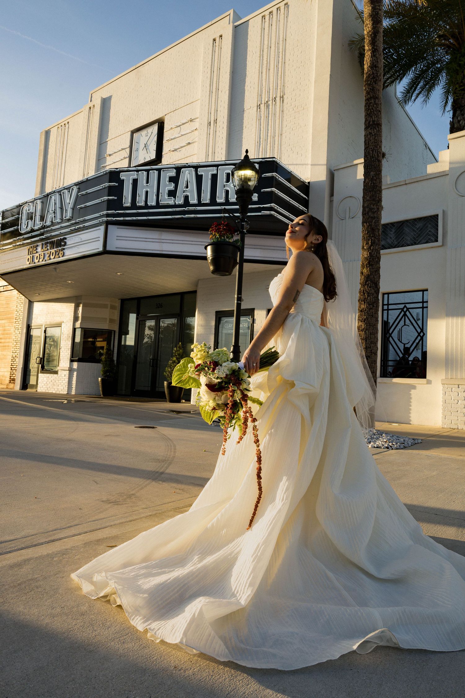Bride in an elegant white ballgown poses dramatically outside a vintage theater building.