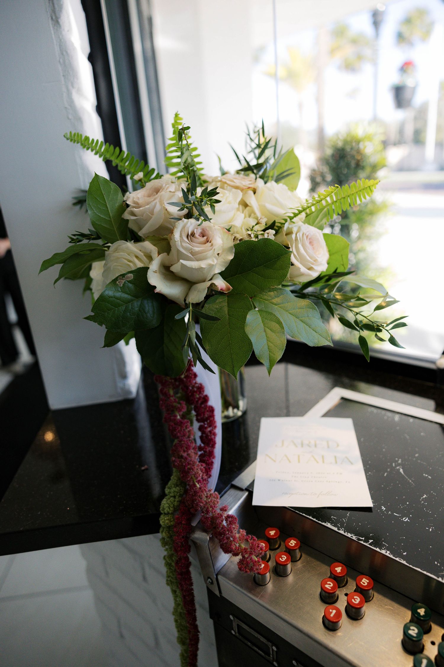 Wedding bouquet with white roses and burgundy accents displayed on dark surface with candles.