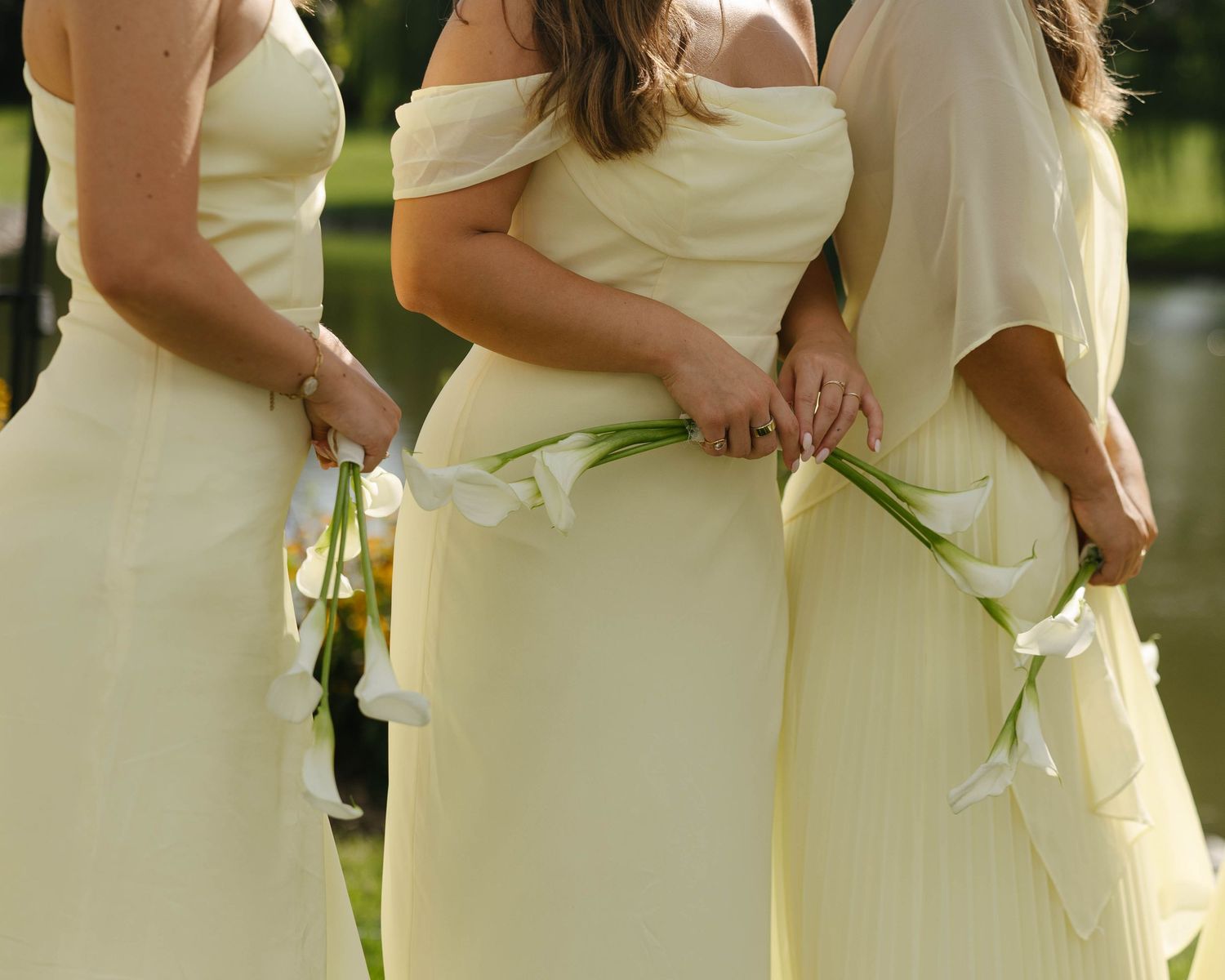 Three bridesmaids in yellow gowns holding white calla lilies at an outdoor wedding ceremony.