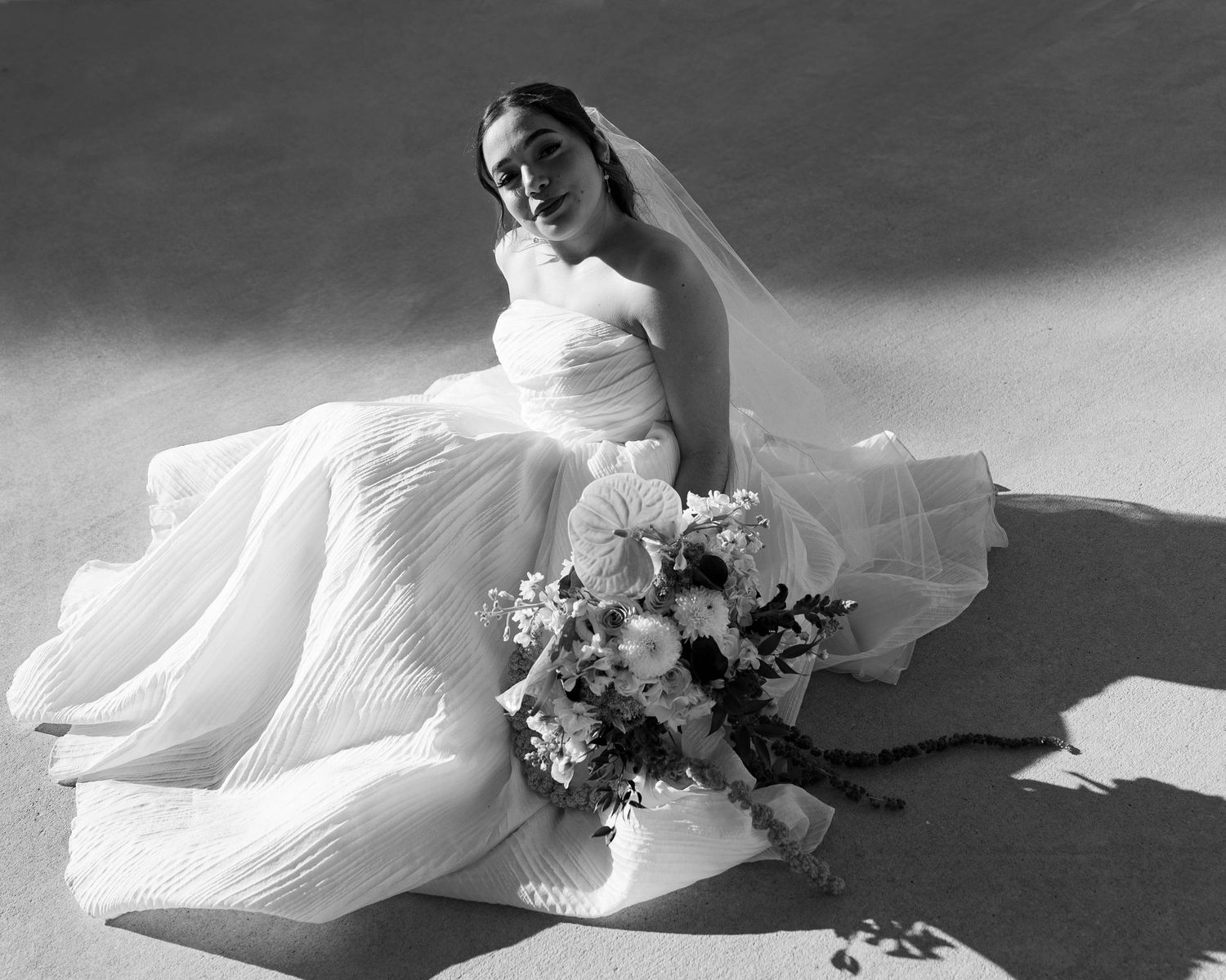 Artistic black and white photograph of flowing white wedding dress fabric with floral details.
