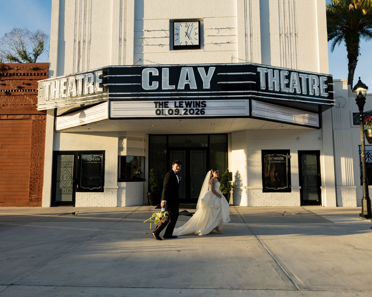 A wedding couple poses beneath the Clay Theatre marquee on their special day.