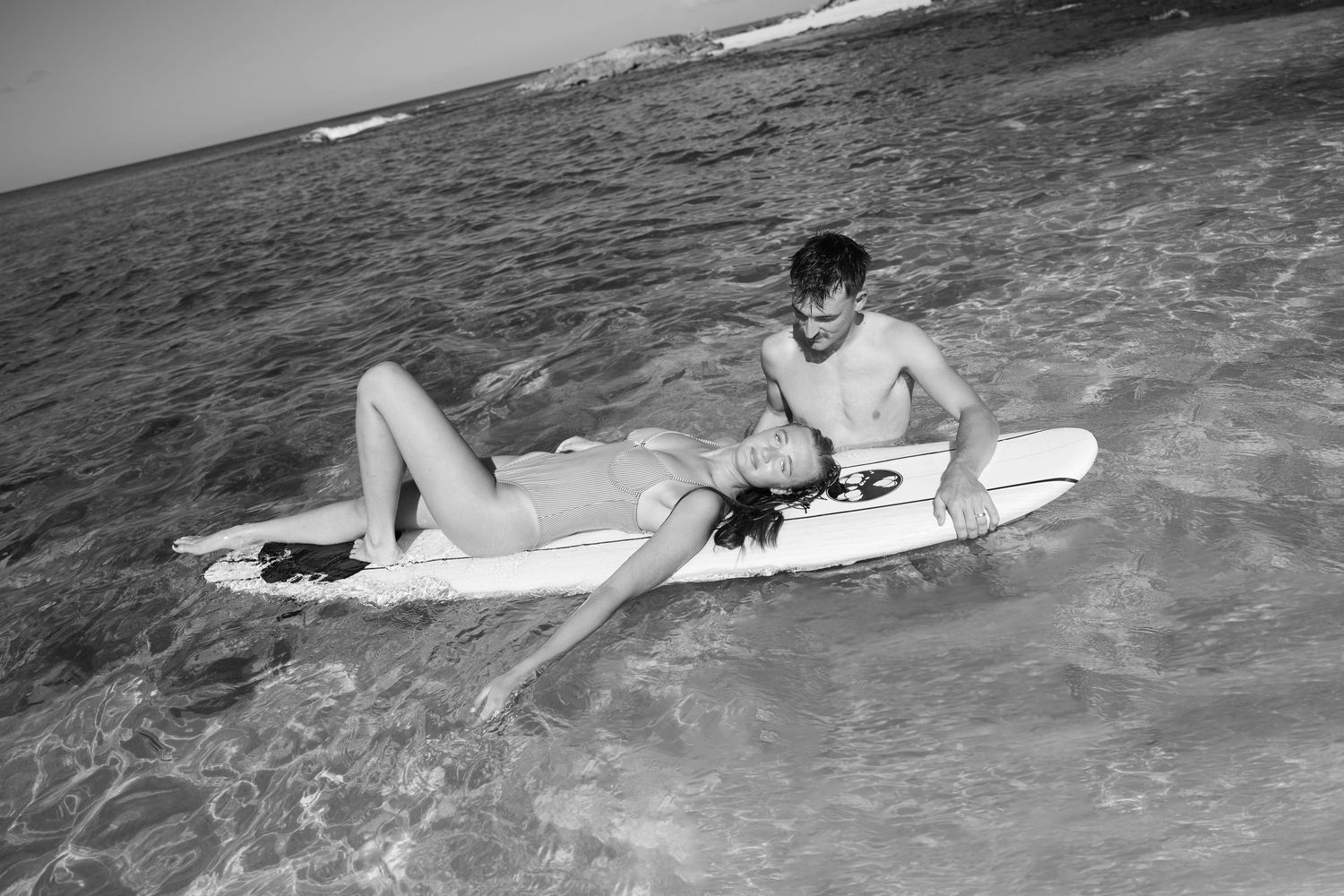 Black and white photo of surfers lounging on boards in gentle ocean waves.