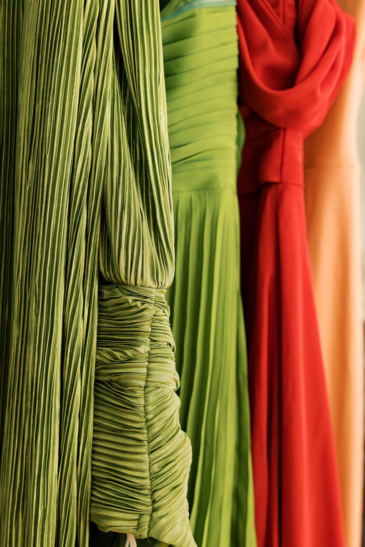 Close-up of pleated bridesmaid dresses in lime green and coral colors hanging together.